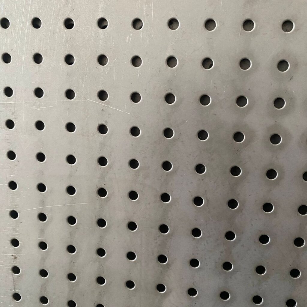 Optimizing Air Pressure with Custom Perforated Metal Sheets - Sudharsun Traders Close-up view of industrial wiremesh rolls stacked in warehouse lighting.